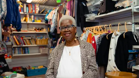 Dueña de una tienda de ropa de barrio sonriendo entre los percheros